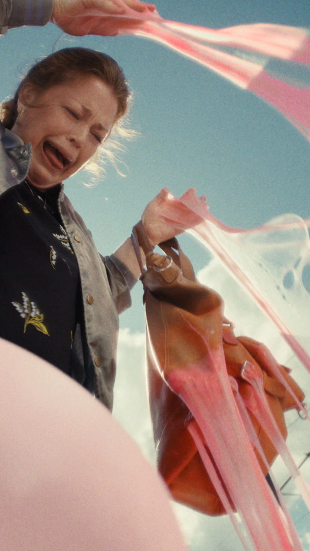 A woman joyfully holds a pink balloon high above her head, smiling in a bright, cheerful setting.