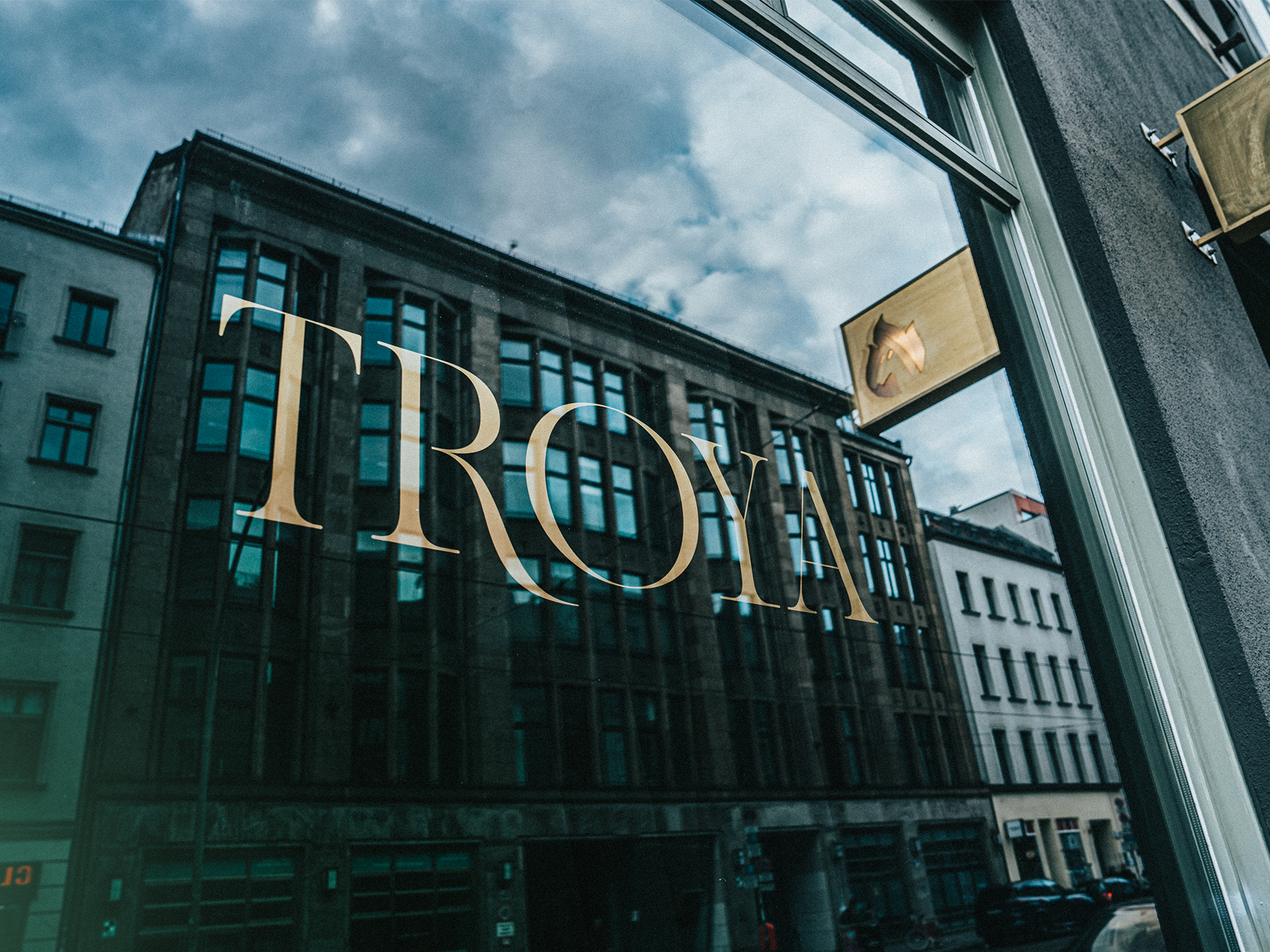 Picture showing a window of the office building of Jung von Matt Berlin Havel in which other buildings are reflected. On the window is the writing "Troya" to read.