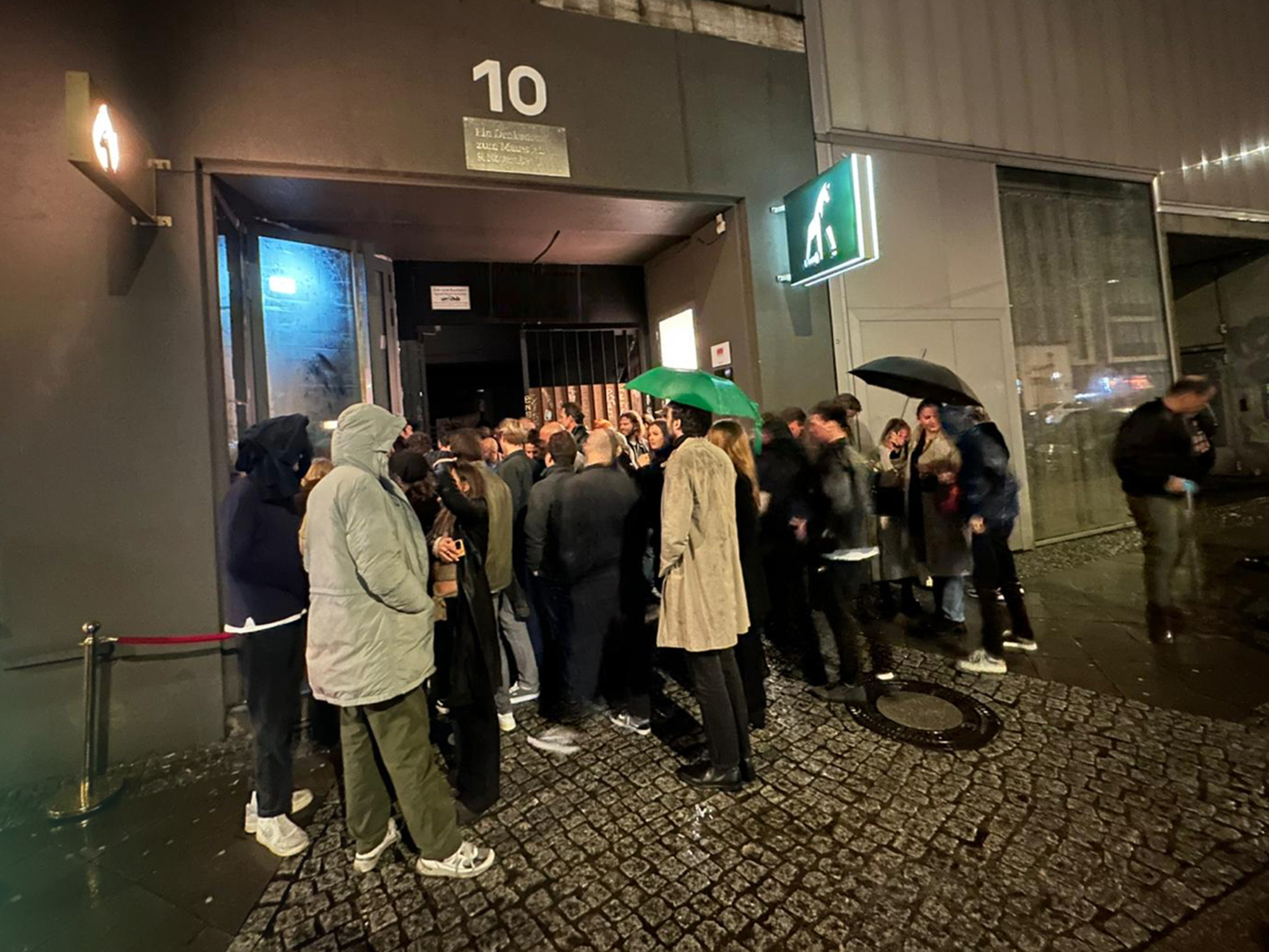 Image of a group of people standing outside of the Jung von Matt Berlin Havel office in the rain. Some of the people holding umbrellas in their hands.