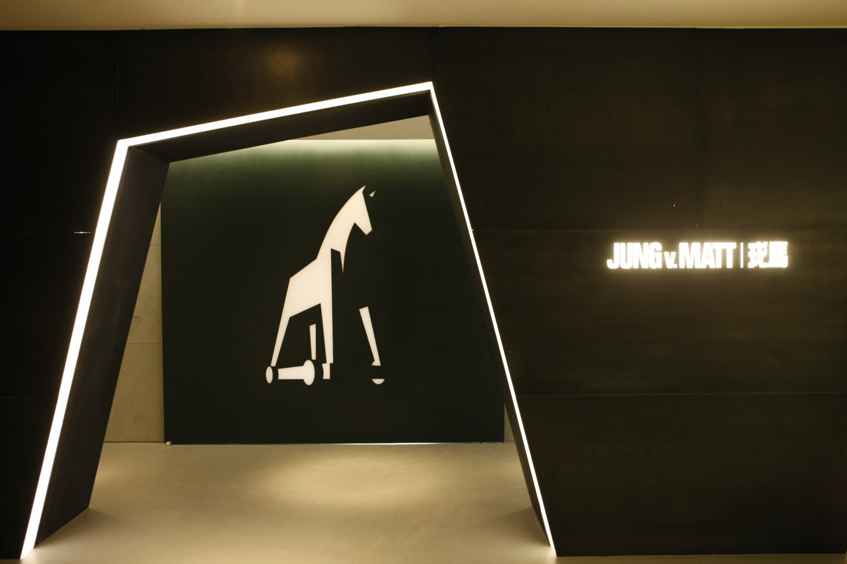 Picture of the modern, futuristic entrance inside the Jung von Matt office building in Beijing. The Trojan horse logo can be seen in the background.