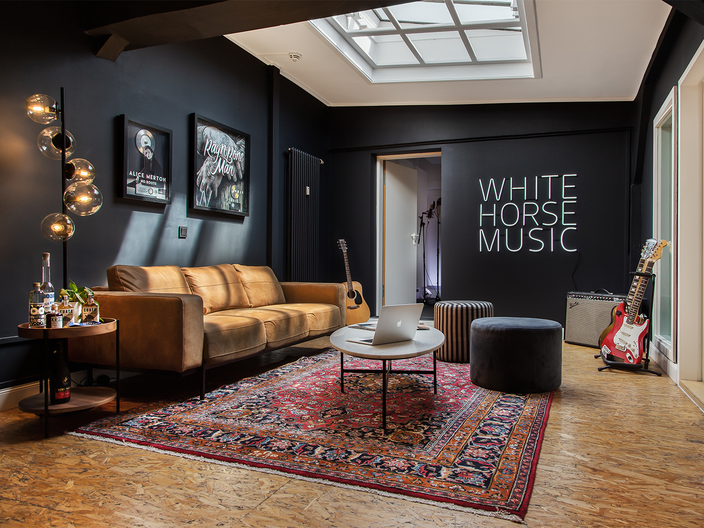 Picture from the inside of the White Horse Music office. Dark walls in a bright room with a sofa and a window on the ceiling. In the corner electric guitars.