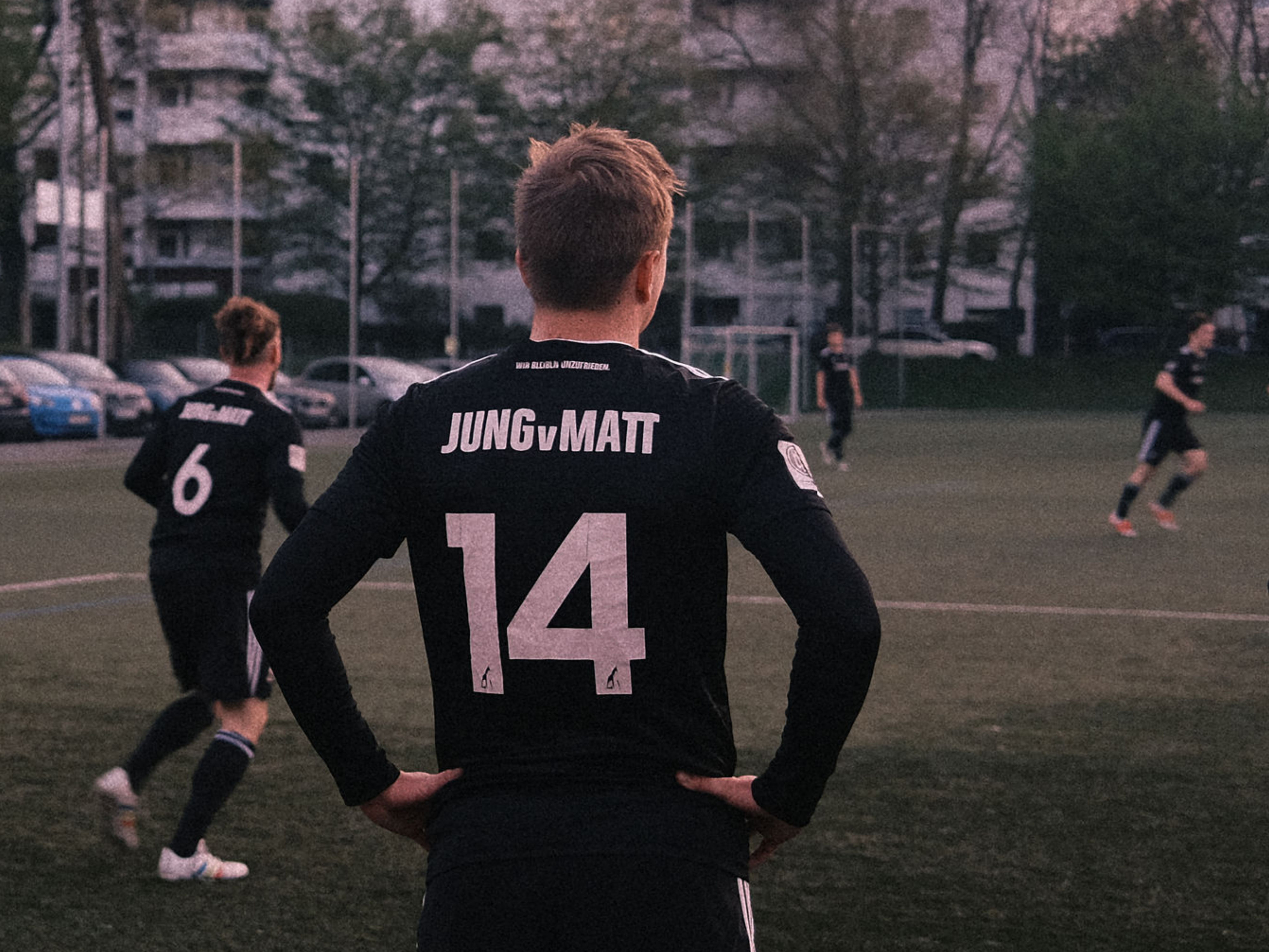 Image of the back of a man on a soccer field. he wears the number fourteen and the saying "we remain dissatisfied" on his jersey.