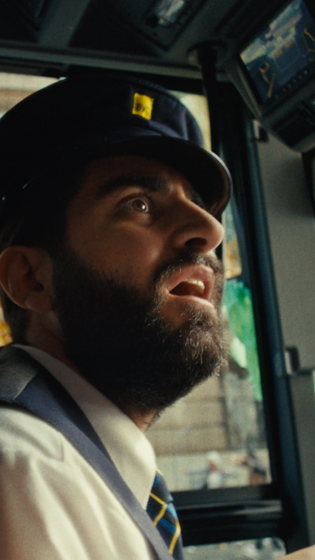  A man in a hat and tie sits comfortably on a bus, looking out the window with a thoughtful expression.  