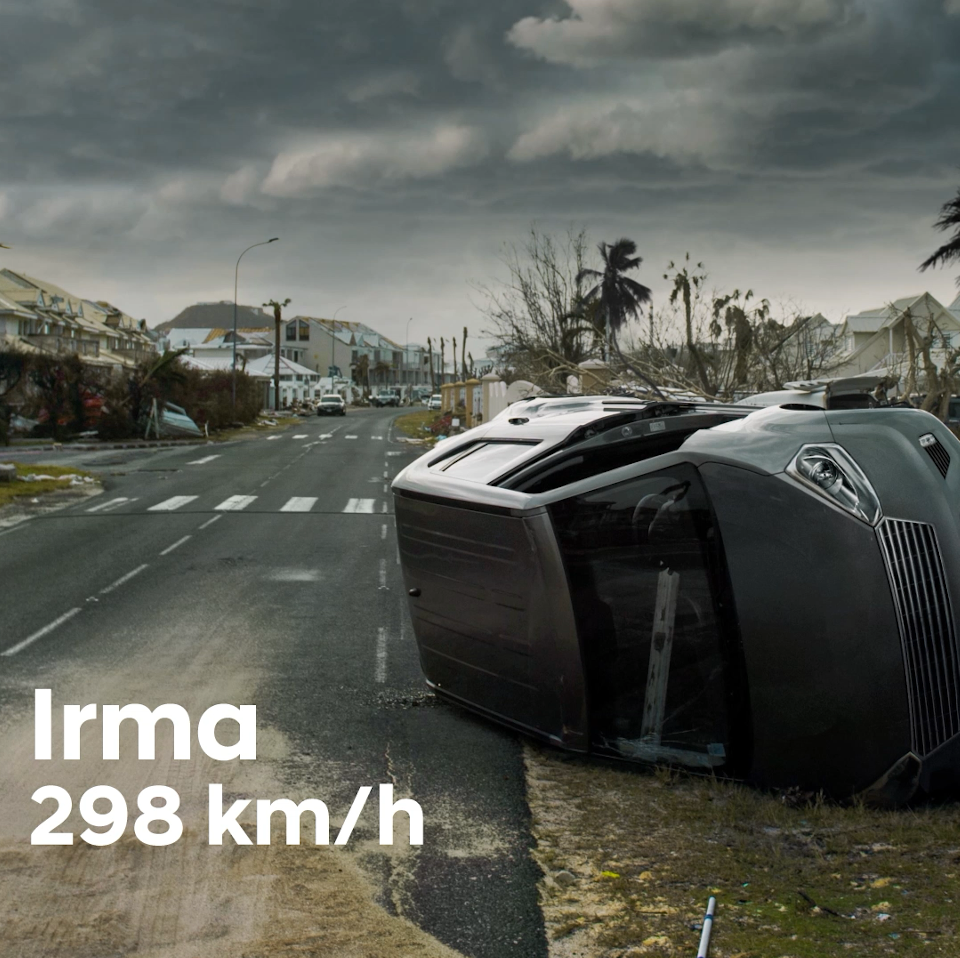 A grey car lying on its side in the middle of a street that has been blown over by hurricane Irma. Caption: Irma 298km/h.