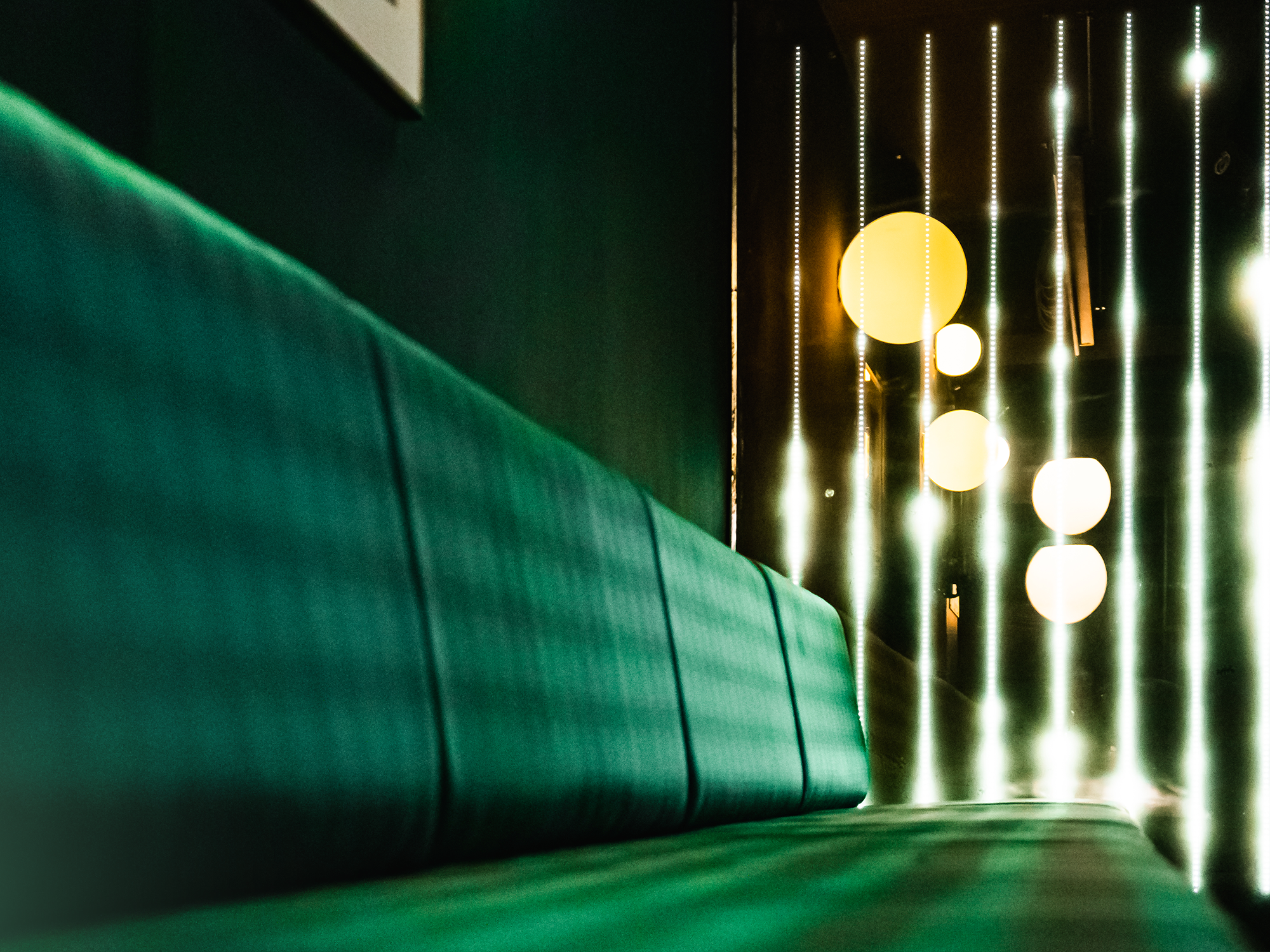 Image of an elongated green sofa-like lounge in the Jung von Matt office Berlin Havel. In the background LED strips and round lamps hanging from the ceiling.