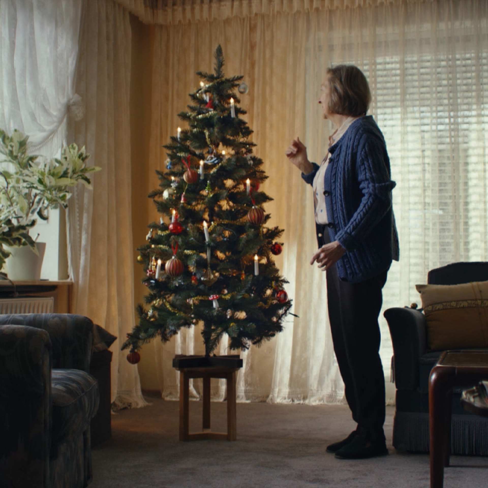 Image of Jung von Matt HAMBURG’s christmas campaign TVC for for retailer chain EDEKA thematising alzheimer's disease: older women with dementia standing in her living room in front of a small decorated Christmas tree with lighted electric candles