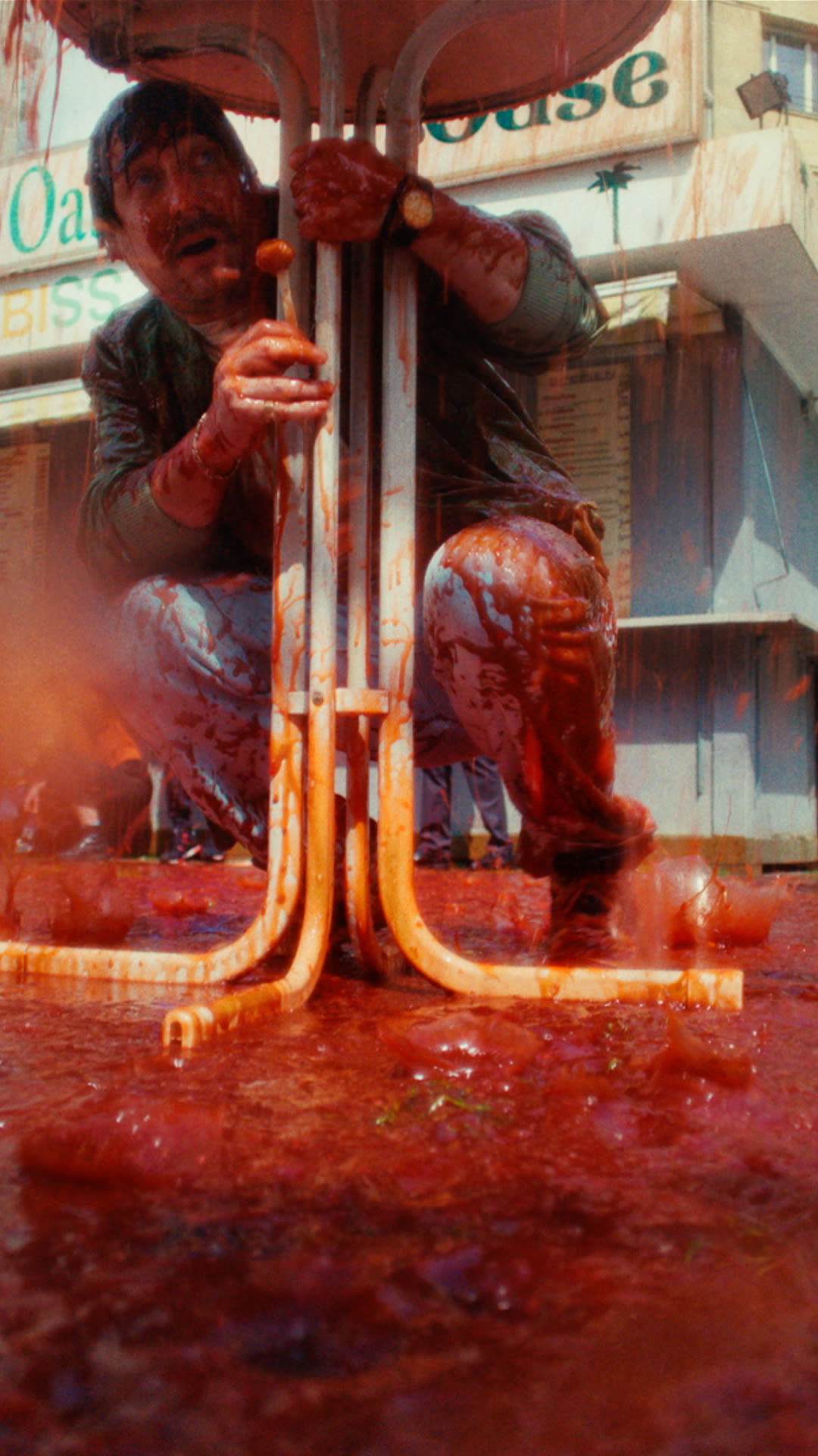 A man kneeling under a table, looking concerned as red liquid spills around him.