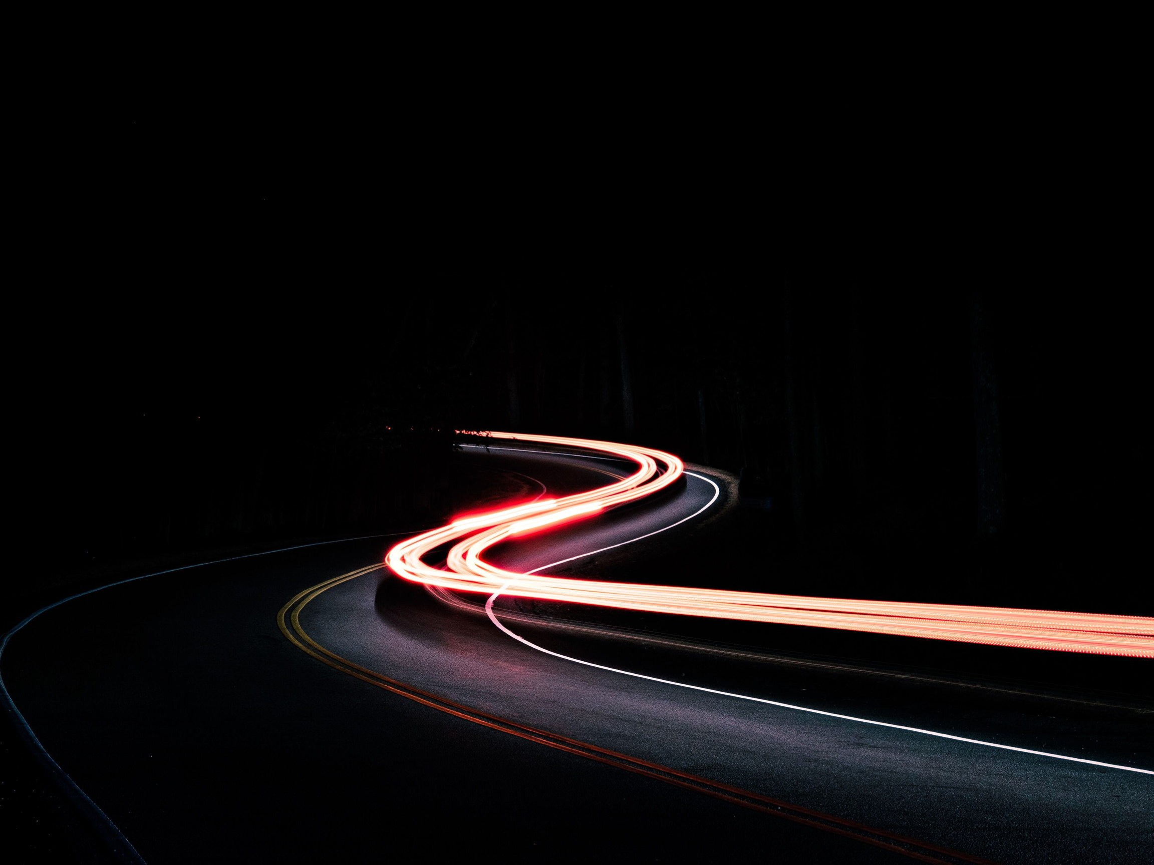 Image of curvy road on black background. On the road are light tails in red.