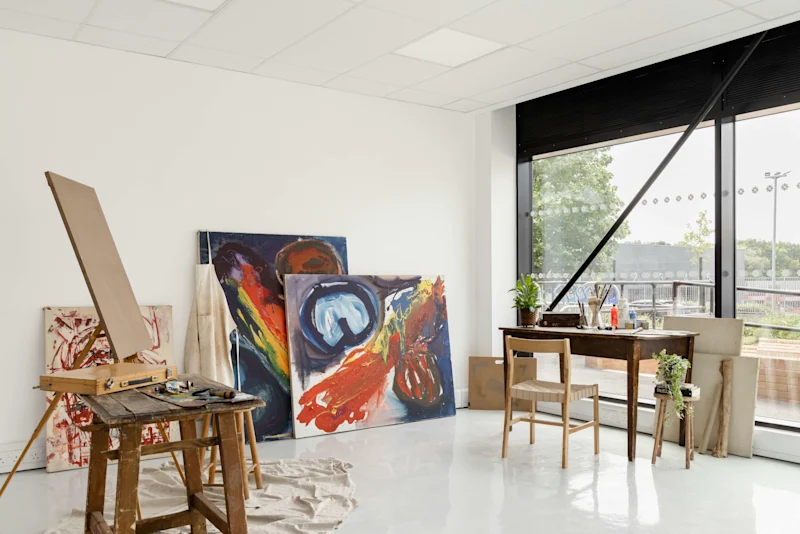 An atelier with finished paintings, a desk and a table with an easel and paint