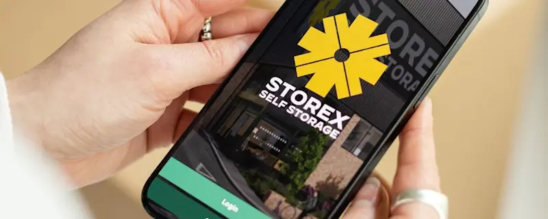 Person holding a smartphone displaying the STOREX Self Storage mobile app login screen for convenient digital access