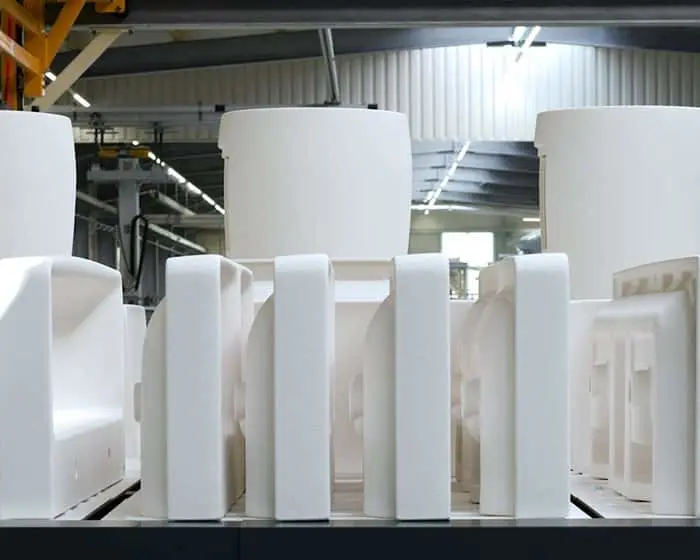 Large white bathroom products and materials arranged in an industrial warehouse with overhead lighting and metal structures.