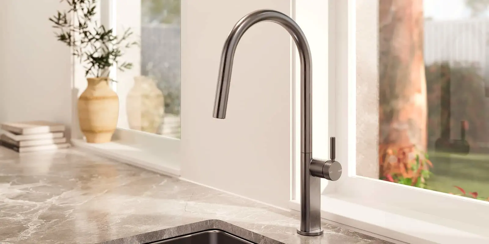 Modern stainless steel kitchen faucet with curved spout on gray countertop near window with vase in background