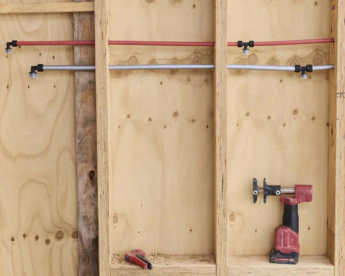 Wooden storage compartments with red and gray pipes mounted horizontally, and a red power drill on the bottom shelf.