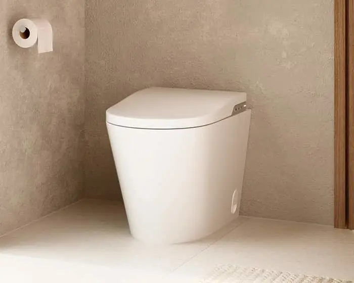 White modern toilet with closed lid in a bathroom corner with beige walls and a toilet paper roll holder.