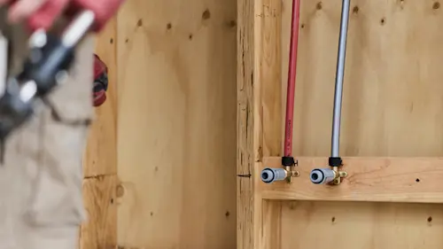 Two water supply lines, one red and one blue, installed through wooden wall framing with shut-off valves.