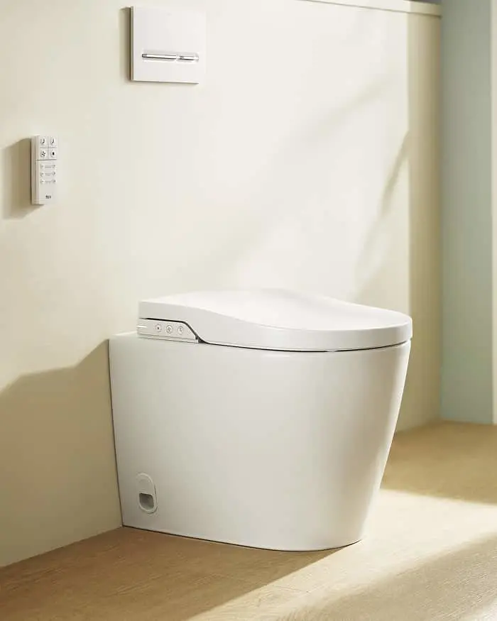 White modern toilet with electronic bidet seat in a minimalist bathroom with light wood flooring and wall controls.