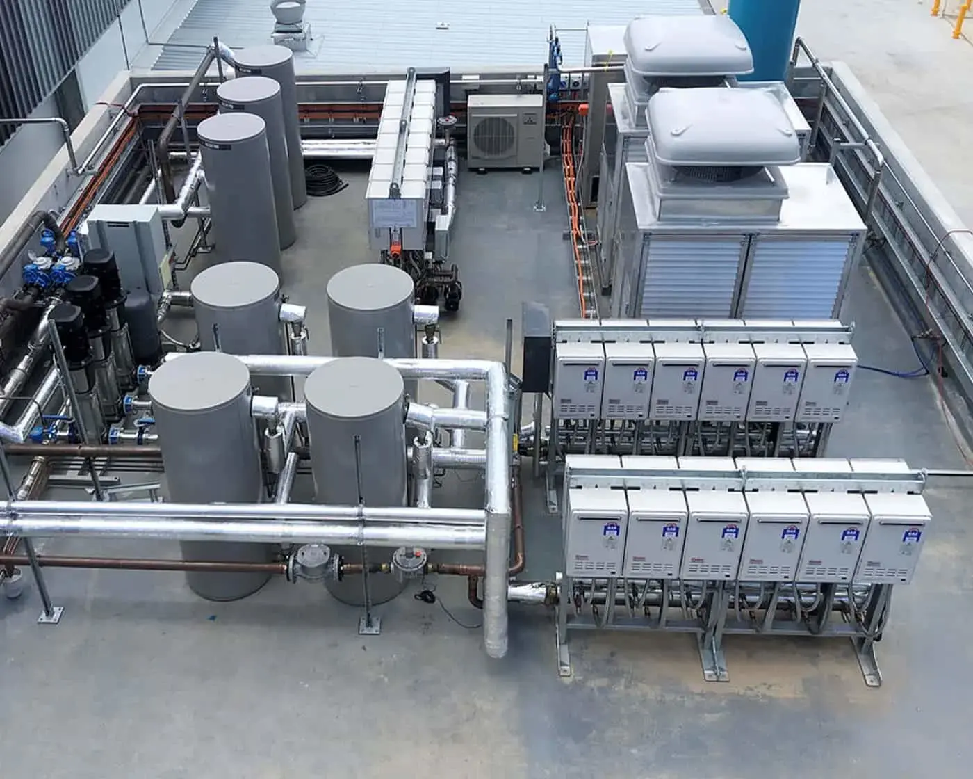 Aerial view of industrial rooftop with HVAC units, white cylindrical tanks, silver piping, and electrical equipment.