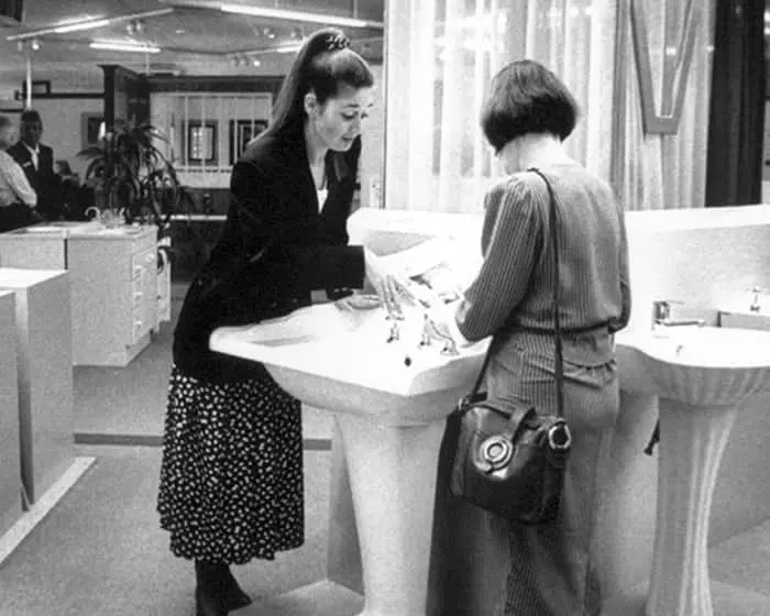 Two women in business attire conversing at a high-top table in a vintage showroom setting.
