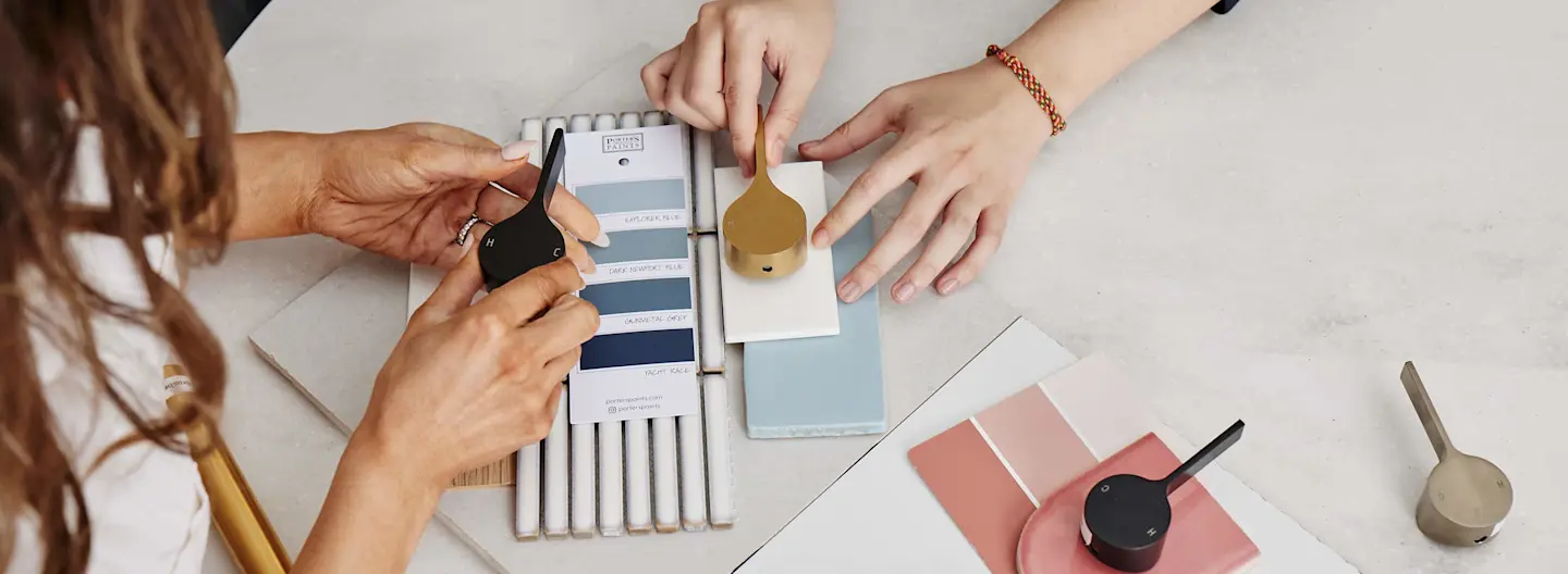 Two people reviewing color swatches and paint samples on a white table with various design materials spread out.