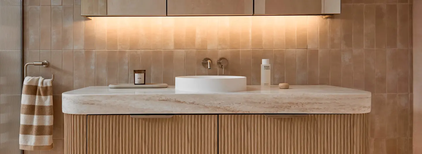 Modern bathroom vanity with white round sink, marble countertop, beige tile backsplash, and striped towel on rack.
