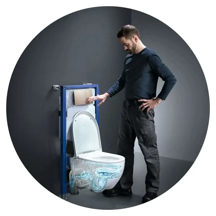 Man in dark clothing demonstrating a wall-mounted toilet with blue frame and visible plumbing against gray background