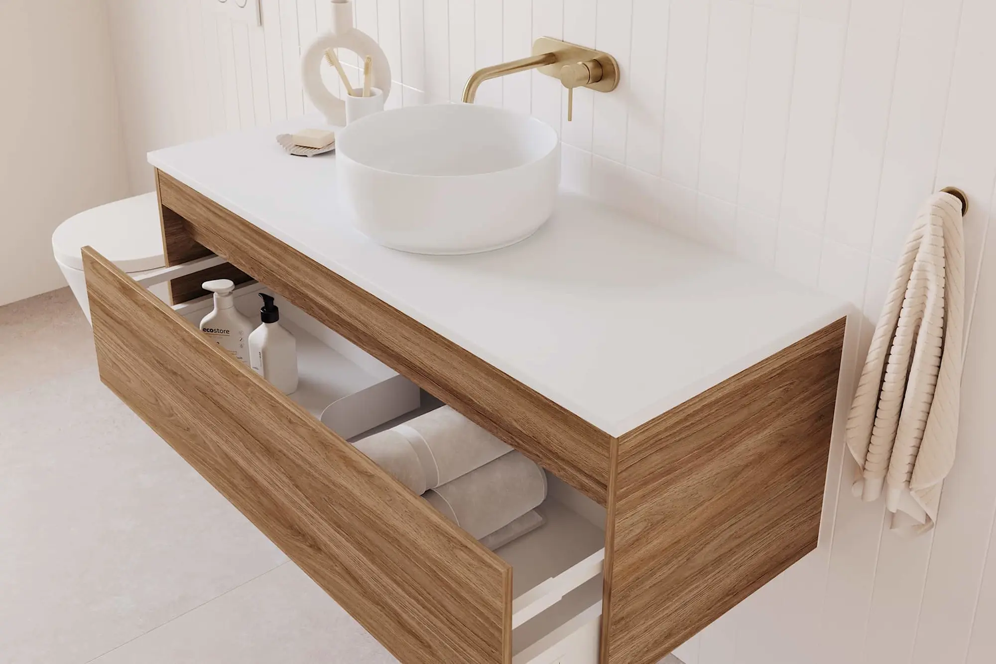 Bathroom vanity with white countertop, round vessel sink, brass faucet, and wood drawer open showing towels inside.