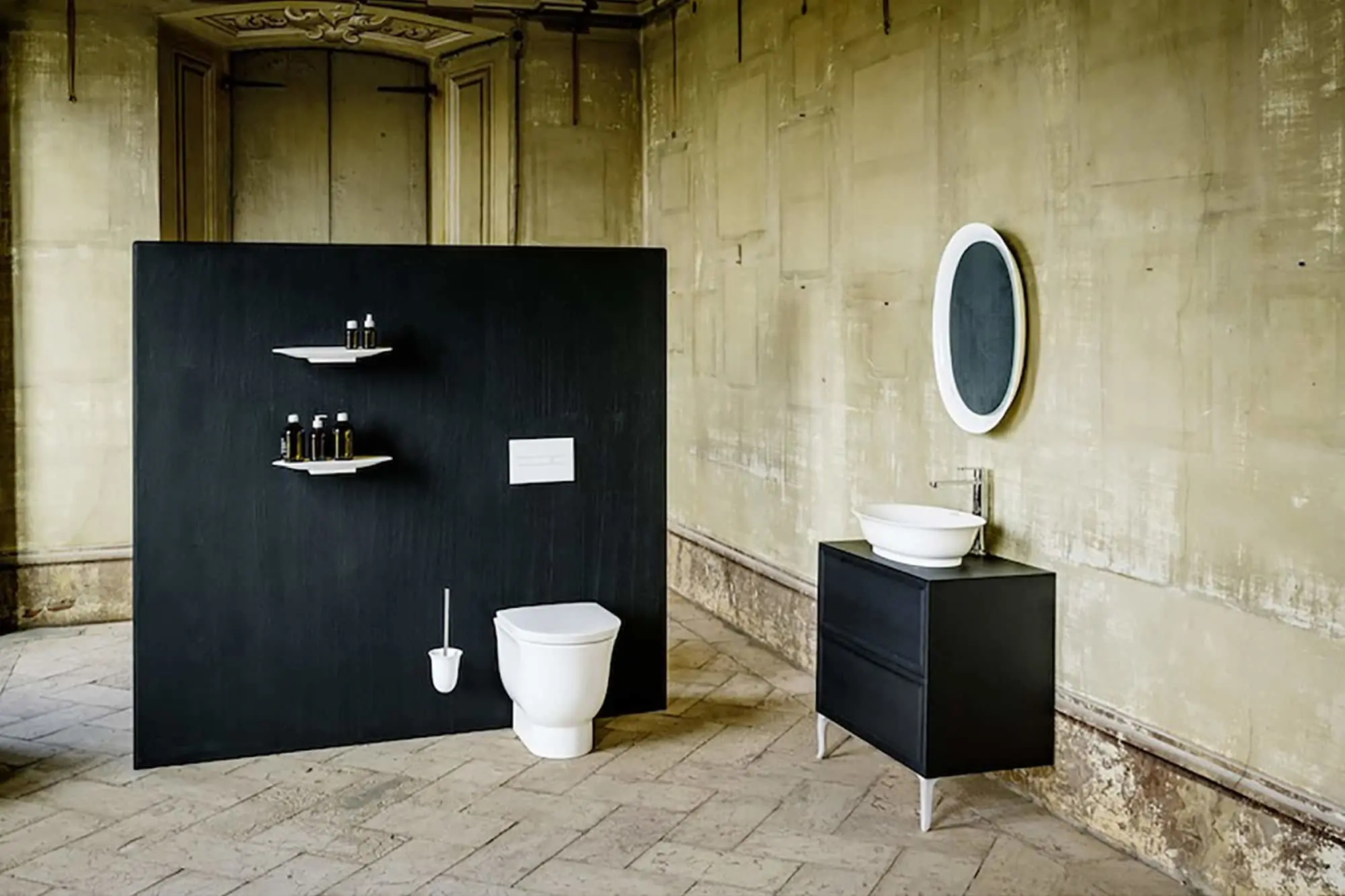White toilet, black vanity, vessel sink, and round mirror against weathered walls.