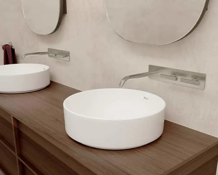 Modern bathroom with two white round vessel sinks on wood countertop, wall-mounted faucets, and round mirrors.