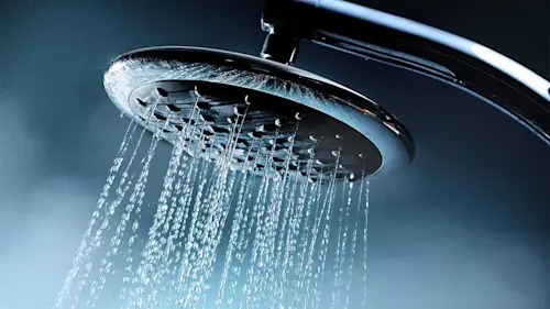Chrome showerhead spraying water against a blue-gray background
