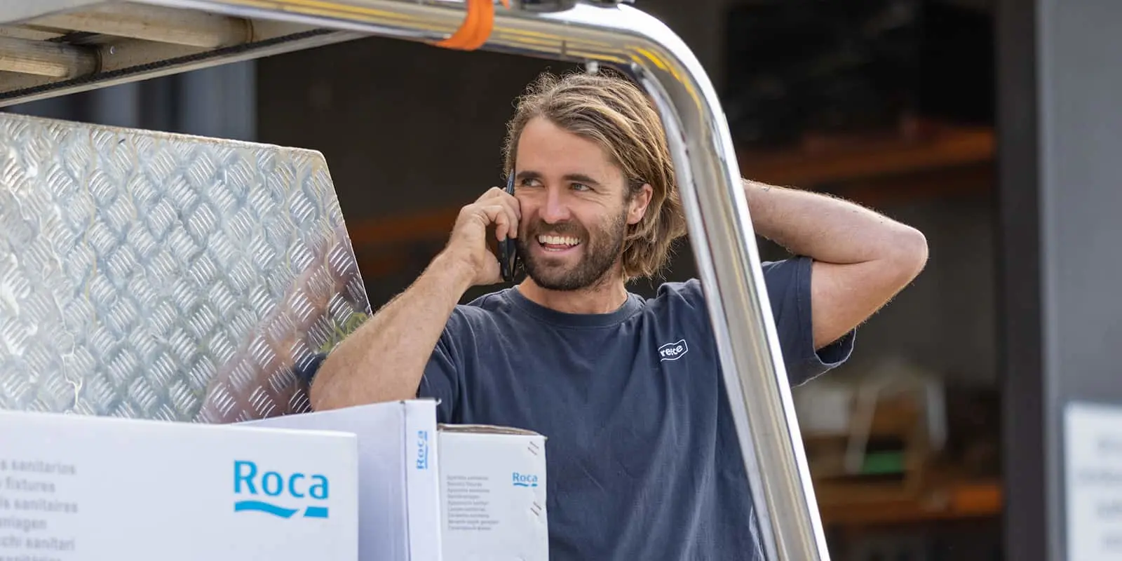 Man in blue shirt talking on phone while sitting in vehicle with Roca boxes visible in foreground.