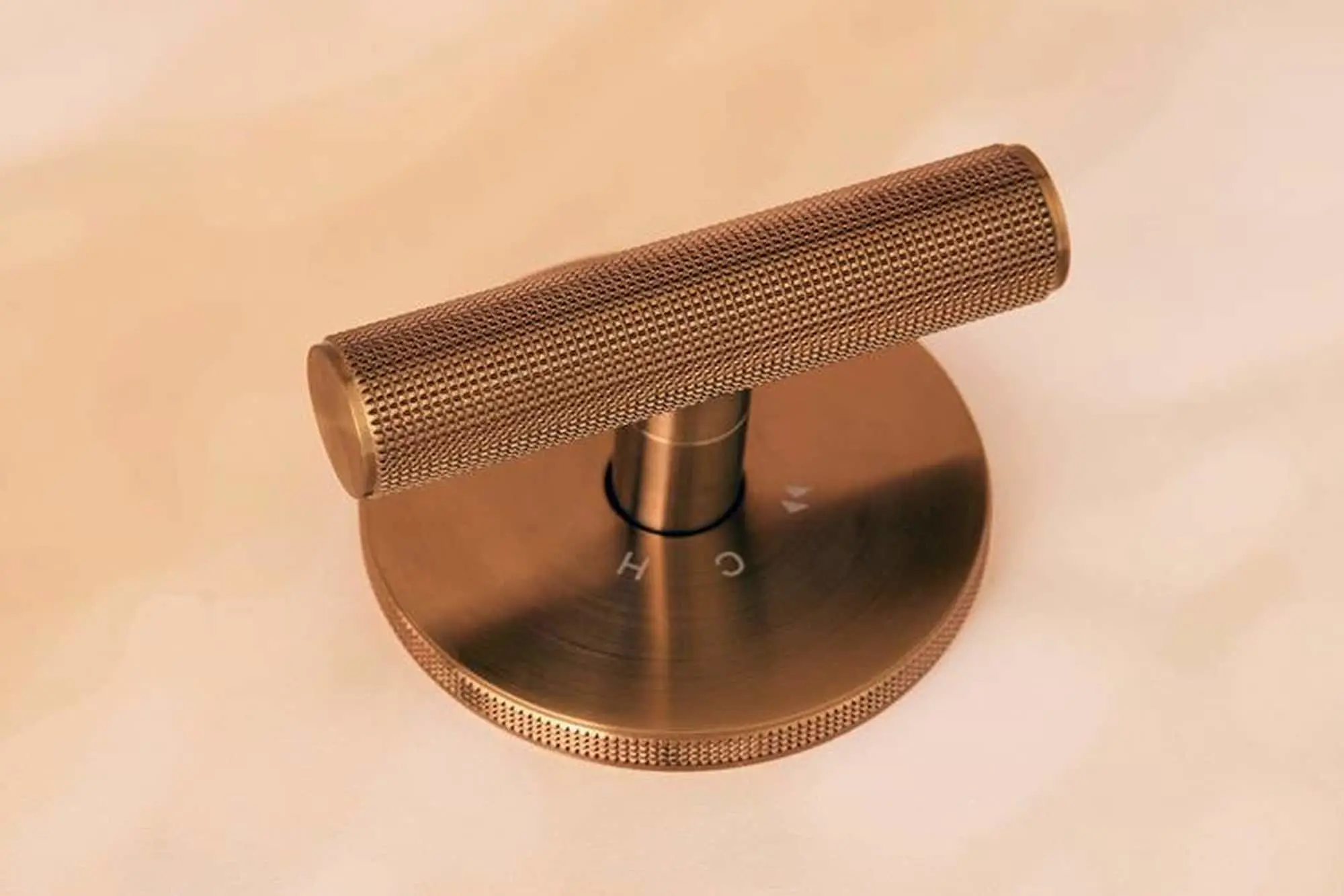 Copper-colored shower mixer with textured grip on circular base plate against beige background.