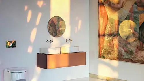 Modern bathroom with white walls, copper floating vanity, two vessel sinks, round mirror, and colorful artwork.