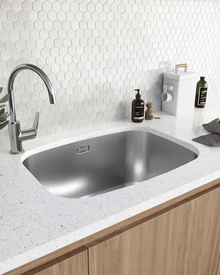 Stainless steel undermount sink in white countertop with chrome faucet and white hexagonal tile backsplash