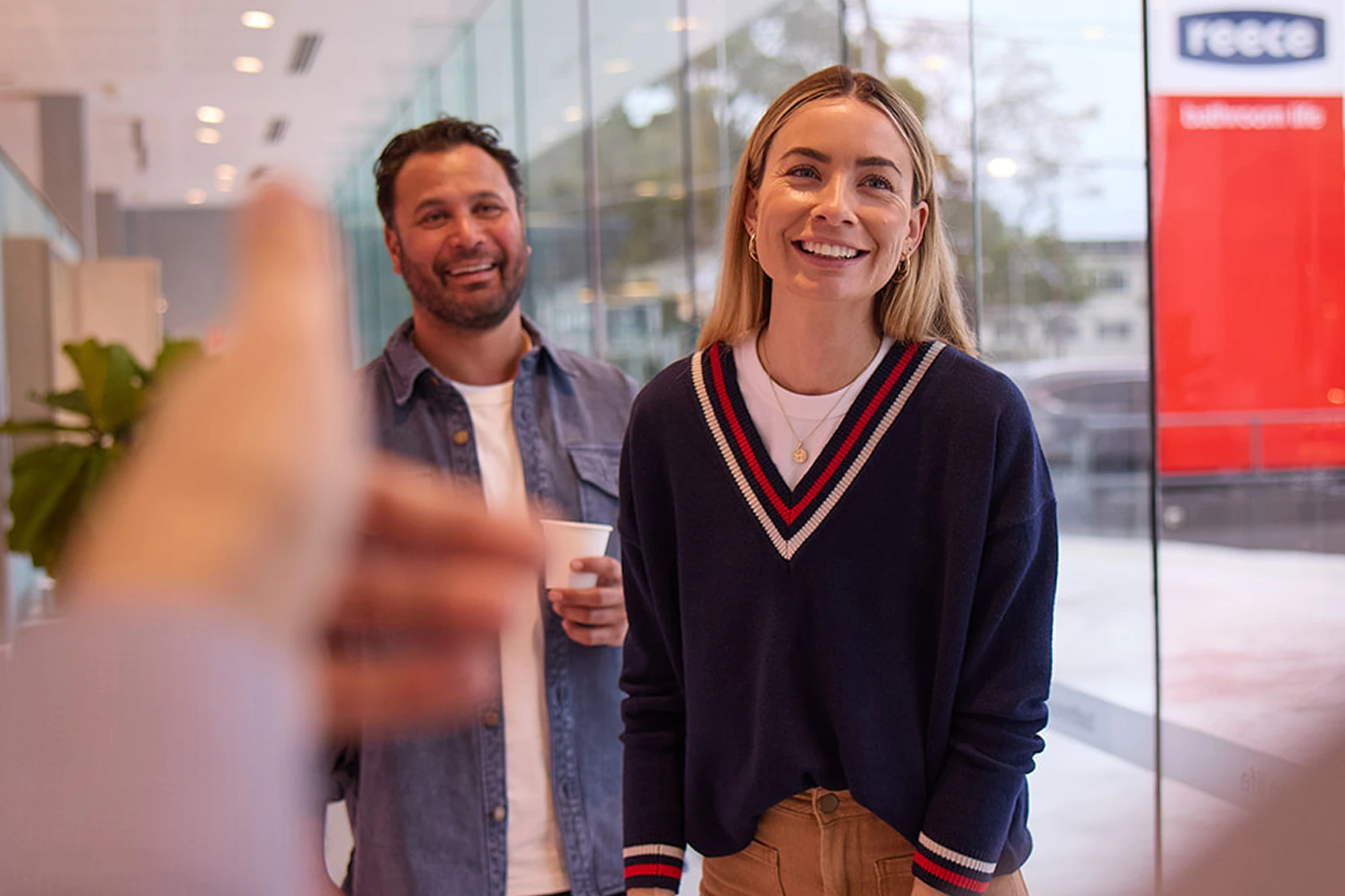 Woman in navy sweater with striped trim smiling in Reece showroom with man in denim shirt behind her.