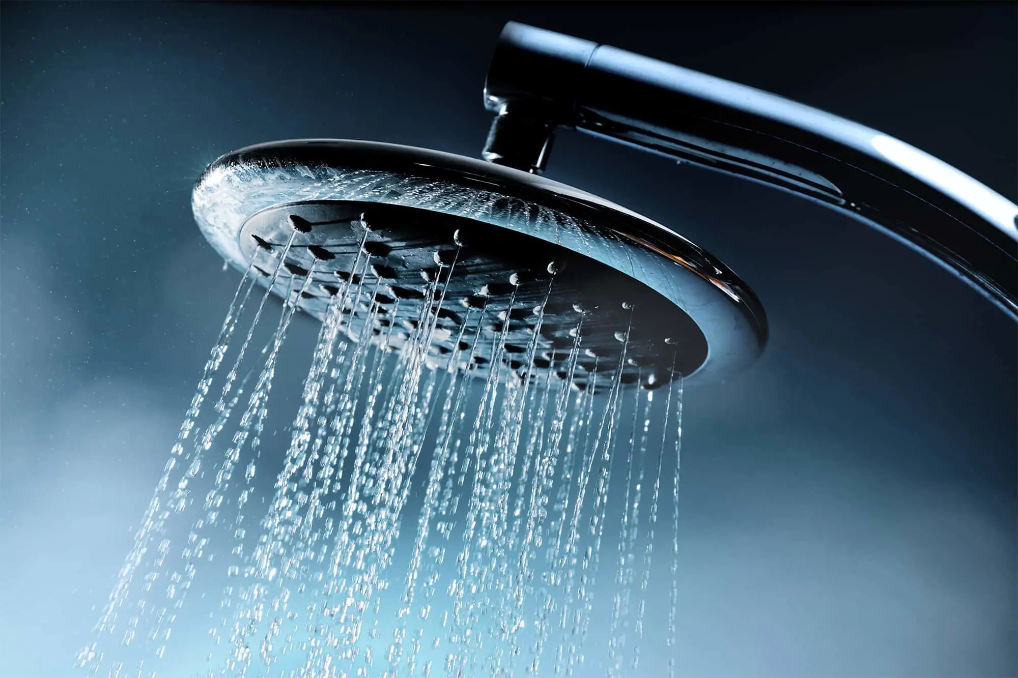 Chrome shower head spraying water against a dark blue background.