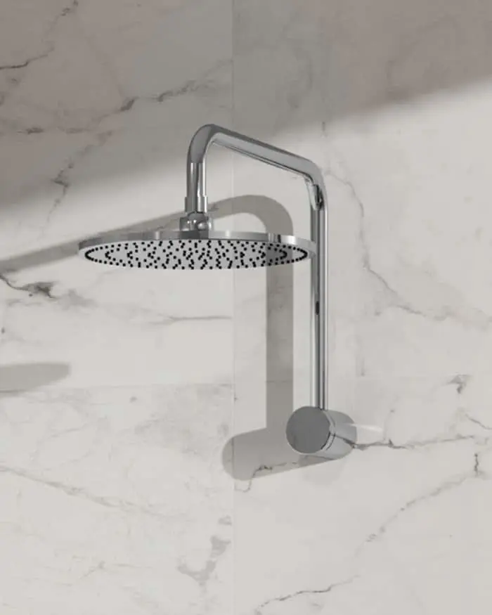 Chrome rainfall showerhead with curved arm mounted on white marble wall