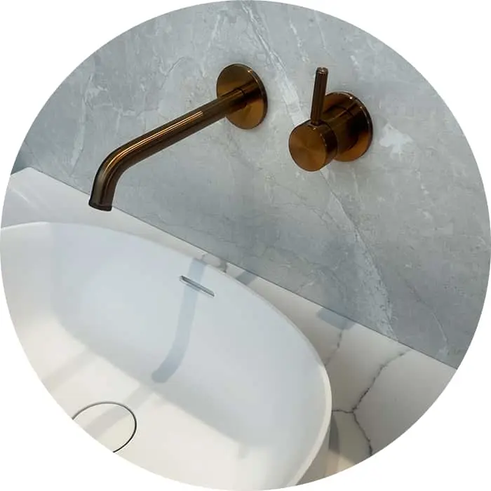 Bronze wall-mounted faucet with spout and handle above white sink against gray marble wall