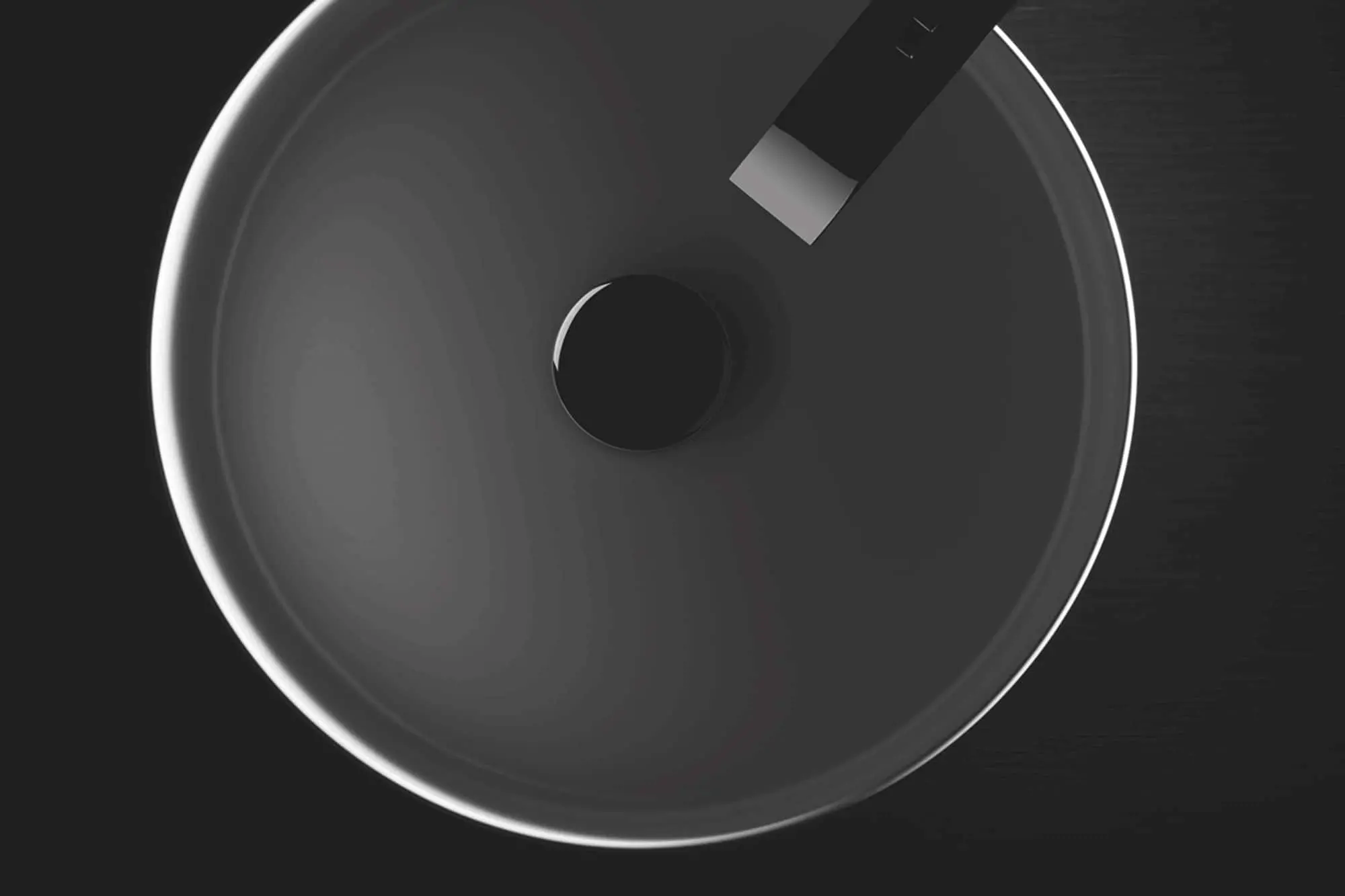 Overhead view of a round dark gray basin with a black faucet against a black background.