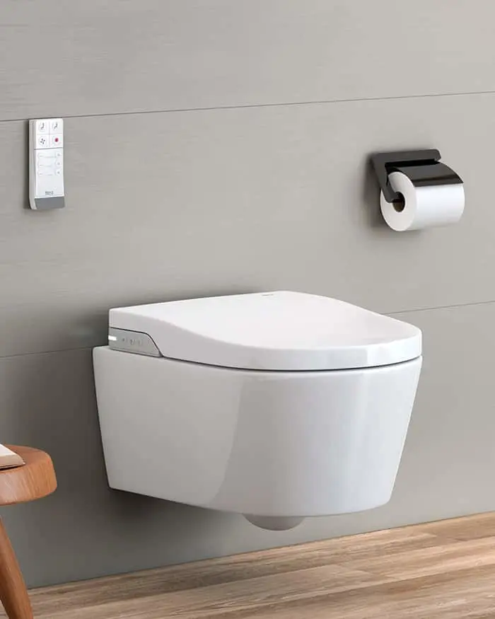 Wall-mounted white toilet with electronic bidet seat, control panel on wall, and toilet paper holder in modern bathroom.