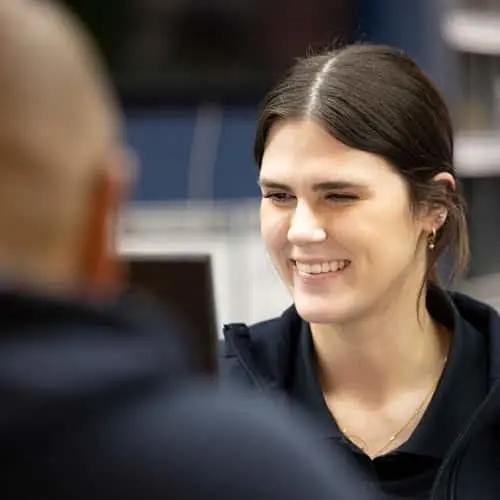 Woman with dark hair smiling while speaking with someone in an office setting