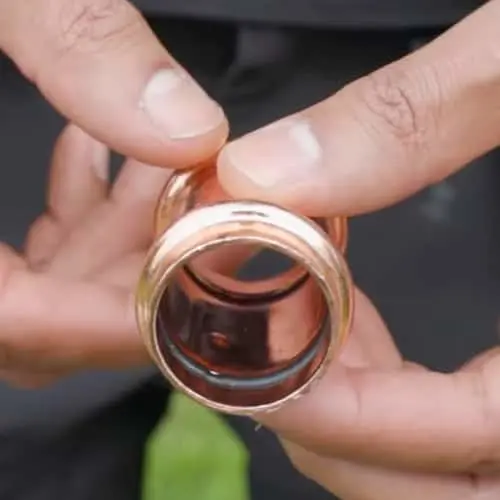 Hands holding a copper pipe fitting above a dark surface.