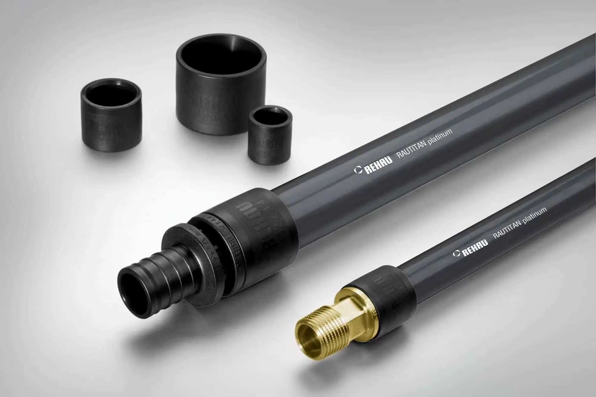 Two gray REHAU RAUTITAN platinum pipes with black and brass fittings, alongside three black cylindrical sleeves.