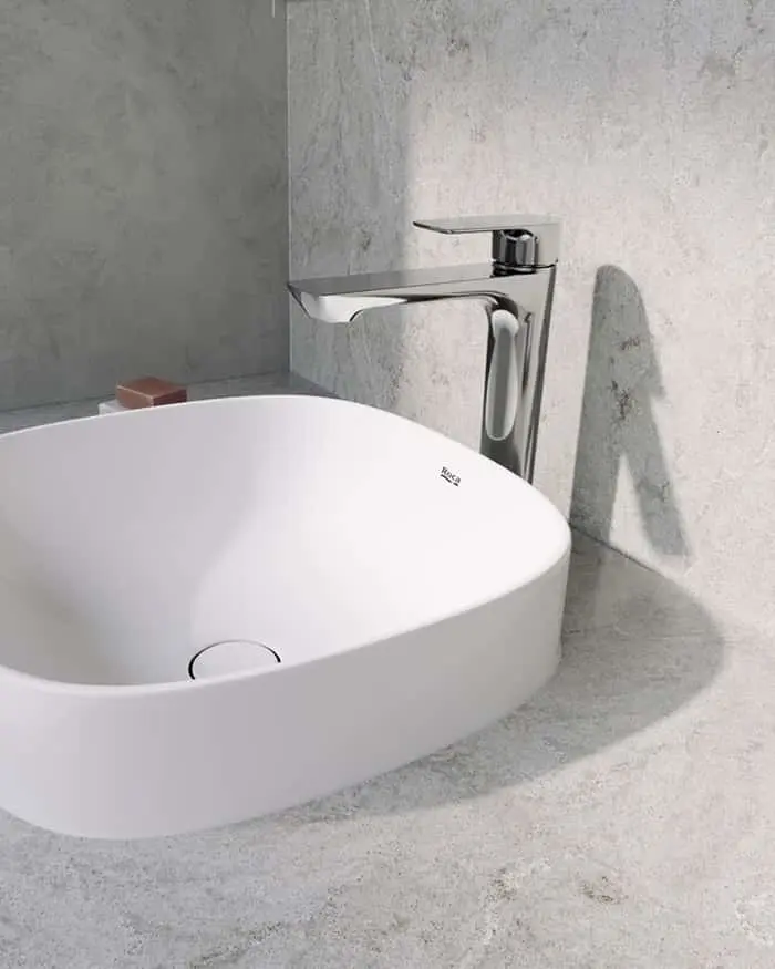 White round vessel sink with chrome faucet on gray concrete countertop against textured concrete wall