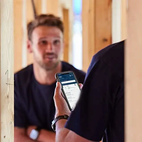 Person holding smartphone displaying app interface in construction site with wooden framing visible in background