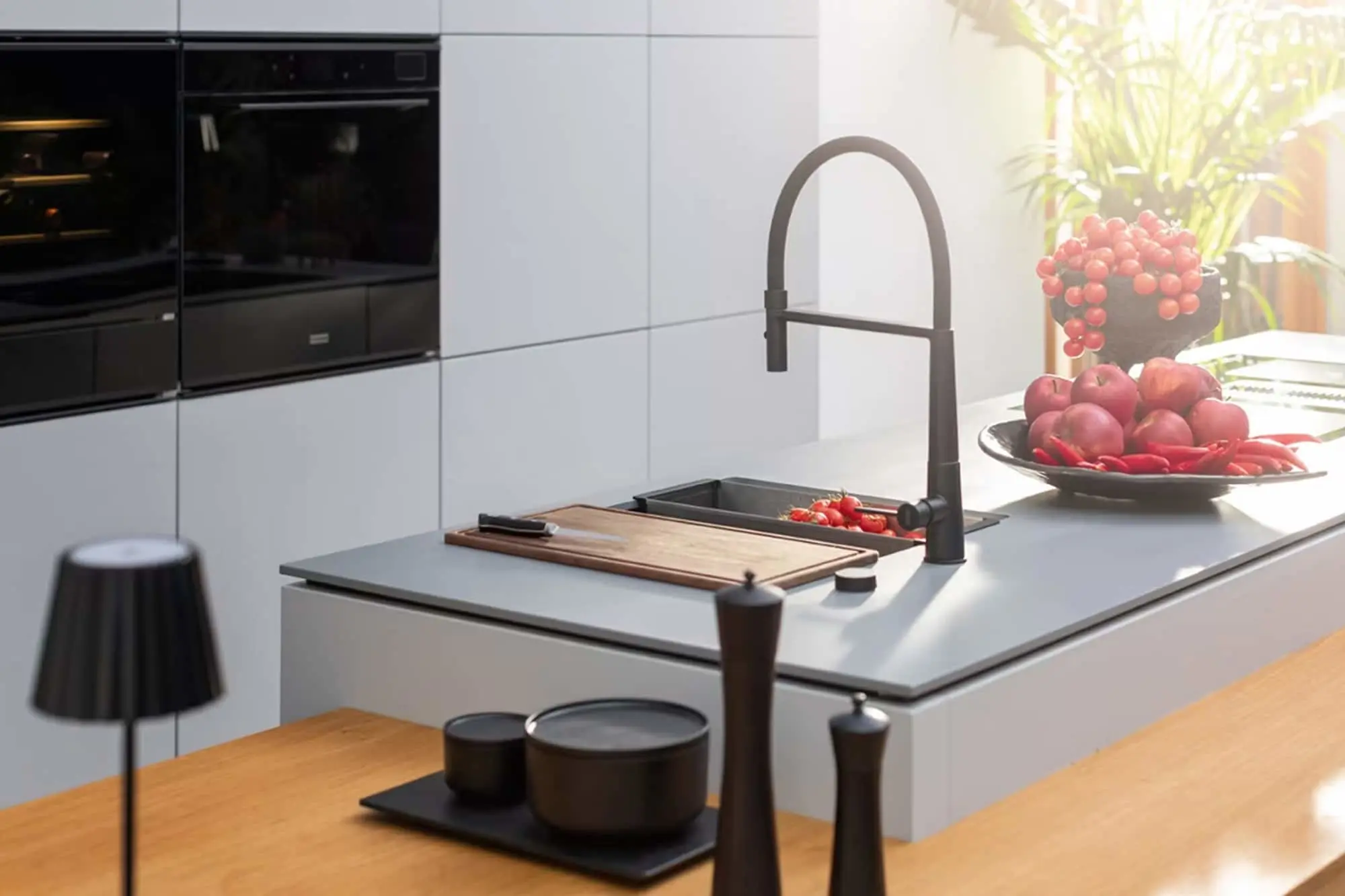 Modern kitchen with white cabinets, black appliances, gray countertop, black faucet, cutting board, and fresh fruit.