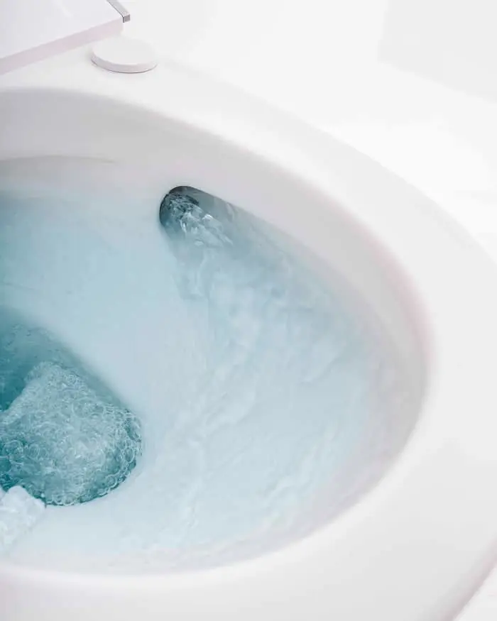 White toilet bowl with blue water swirling during flush, viewed from above.