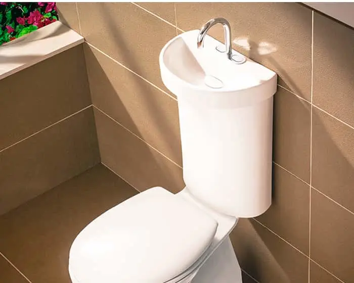 White toilet with integrated sink on top against brown tiled bathroom wall