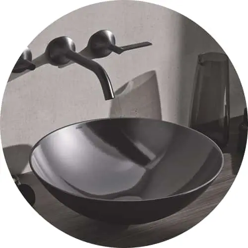 Modern black vessel sink with matching wall-mounted faucet on a concrete countertop in a minimalist bathroom setting.