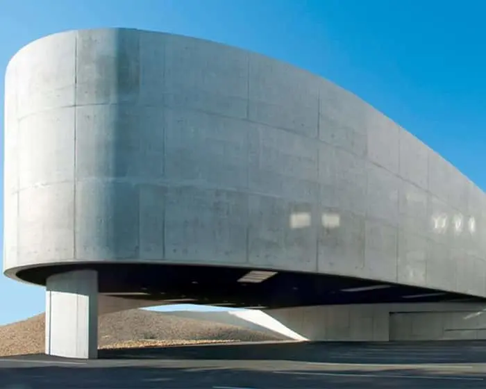 Modern concrete building with curved cylindrical design elevated on white pillars against a blue sky.