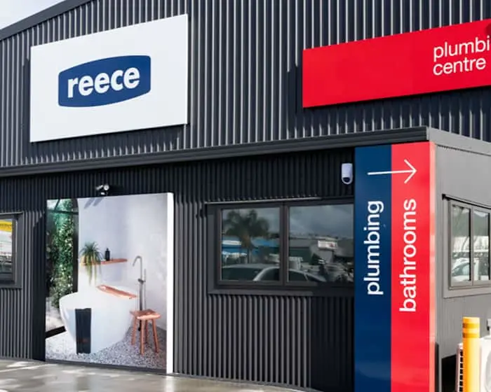 Exterior of a Reece plumbing and bathroom store with corrugated metal siding and directional signage